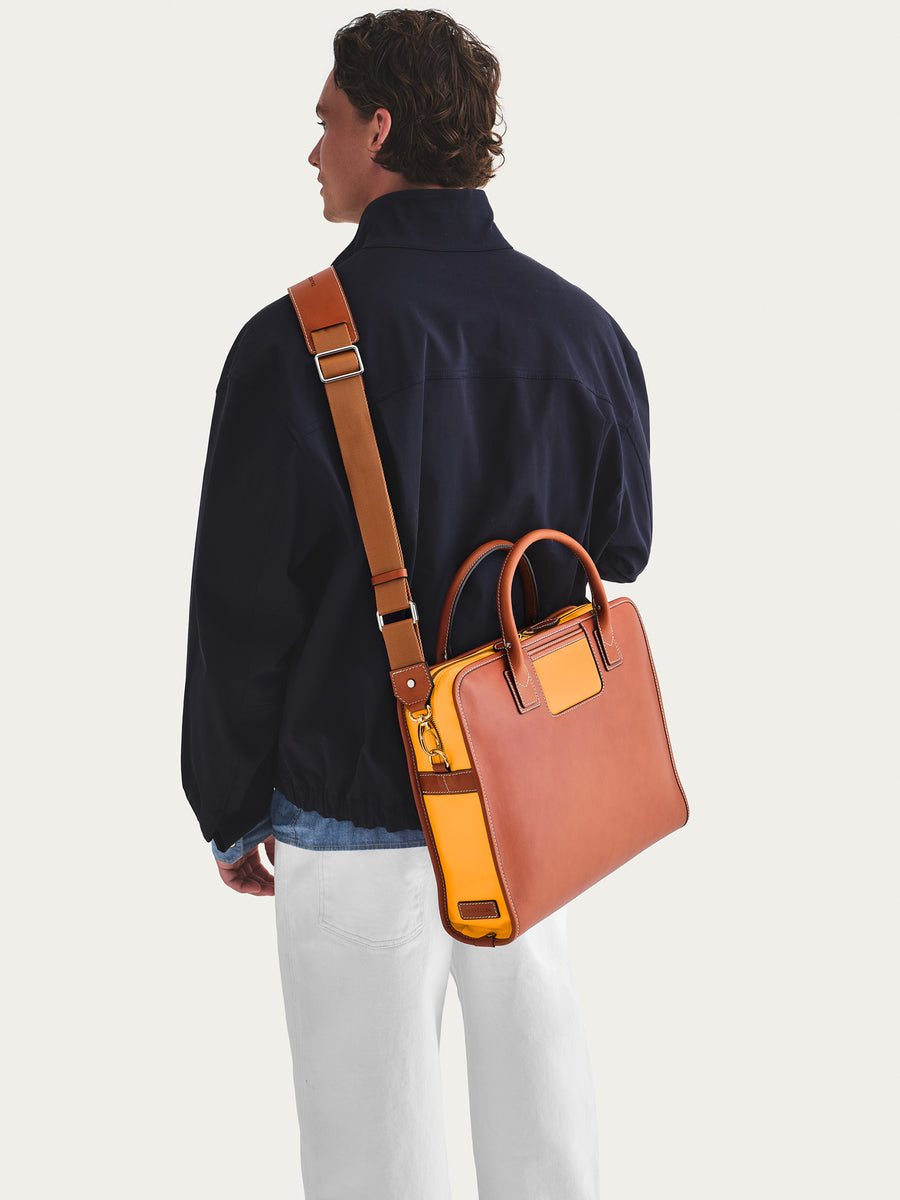 Person carrying a orange leather briefcase with a strap over shoulder on a white background.