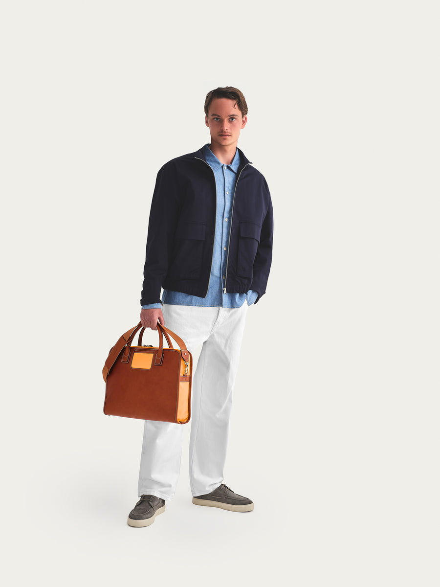 Man holding a brown leather bag against a plain background