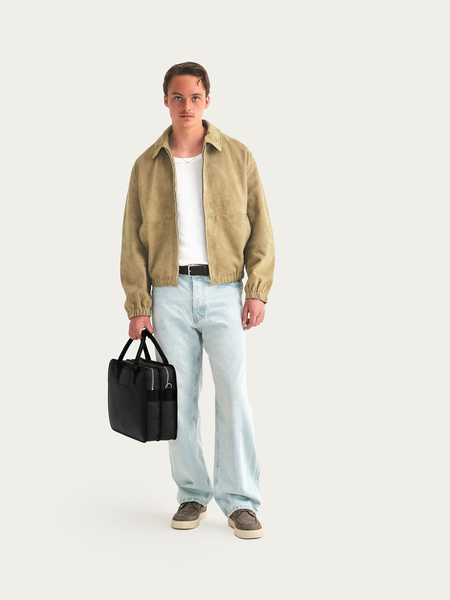 Man holding a black briefcase wearing a beige shirt, white t-shirt, light blue jeans, and dark shoes on a white background