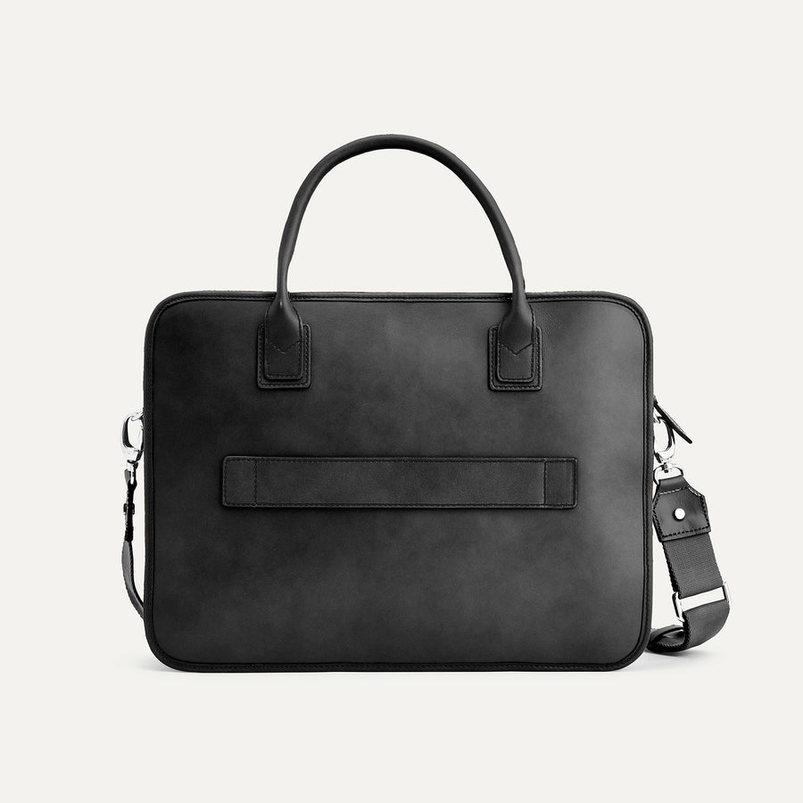 Black leather briefcase with shoulder strap on a light gray background
